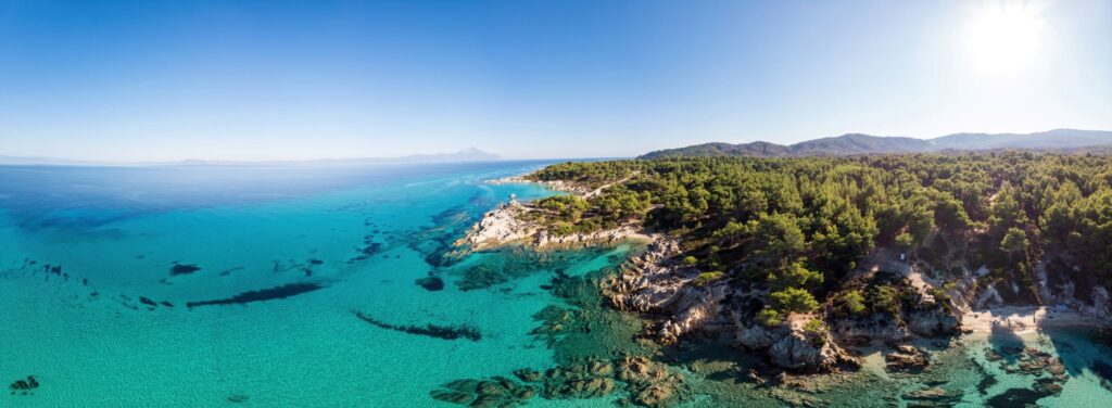 Costa Mar Egeo Agua Azul Transparente Vegetacion Alrededor Rocas Arbustos Arboles Vista Zumbido Grecia 1024x376